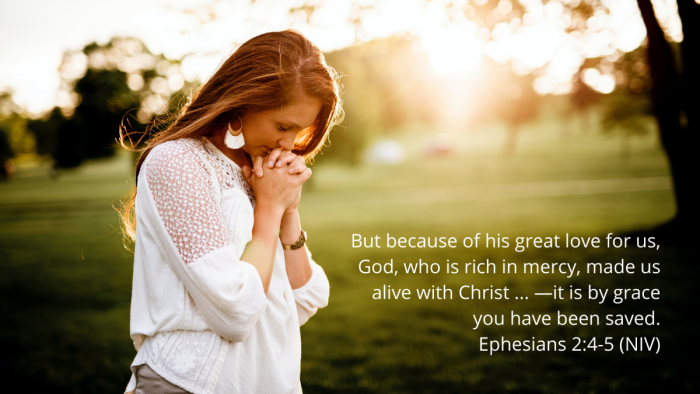 woman praying in a park at sunrise with quotation of Ephesians 2:4-5, NIV
